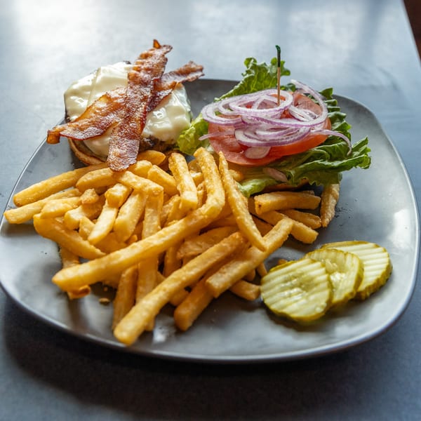 Ollie's Restaurant's bacon cheeseburger with fries and pickles on a gray plate.