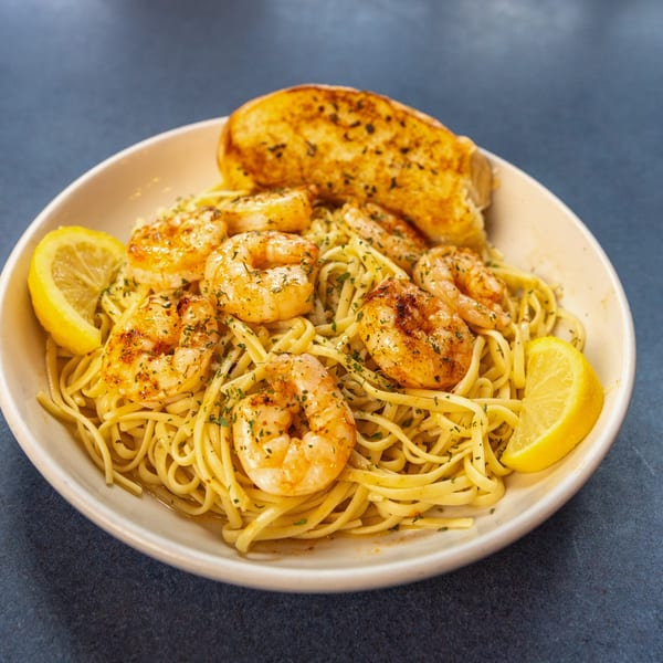 Shrimp scampi with linguine, garlic bread, and lemon wedges in a white bowl at Ollie's Restaurant.