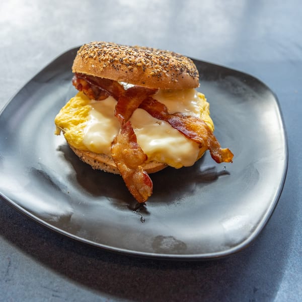 Ollie's Restaurant's breakfast bagel with scrambled eggs, melted cheese, and crispy bacon on a black plate.