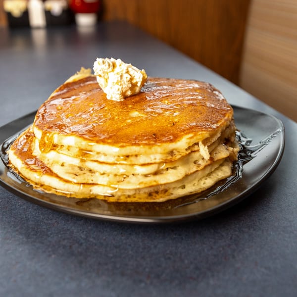 Stack of golden pancakes with melting butter and syrup on a black plate at Ollie's Restaurant.