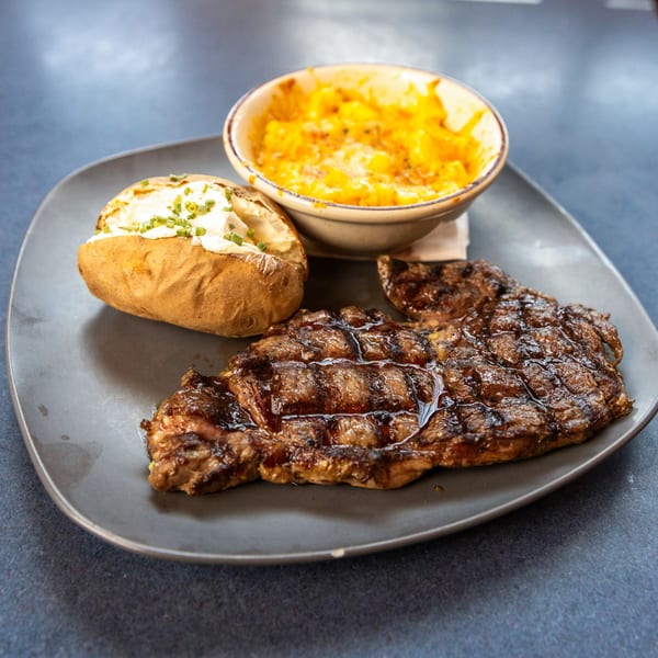 Grilled steak, a loaded baked potato with chives, and a side of macaroni and cheese.